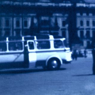 Vintage bus in urban square with pedestrians.