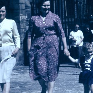 Three women and a child walking together outdoors in vintage clothing.