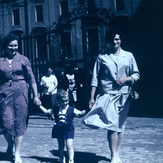 Three women and a child walking together outdoors in vintage clothing.