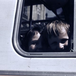 Two children looking out of a moving vehicle window.