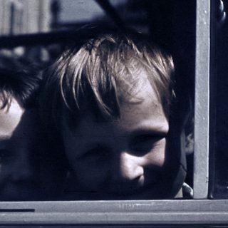 Two children looking out of a moving vehicle window.