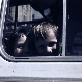 Two children looking out of a moving vehicle window.