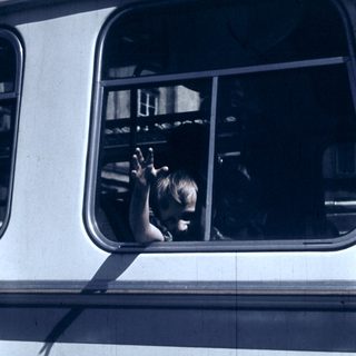 Child waving from a moving bus window.