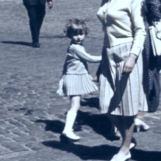 People walking in a cobblestone street, mid-20th century.