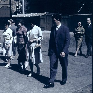 People walking in a cobblestone street, mid-20th century.