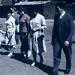 People walking in a cobblestone street, mid-20th century.