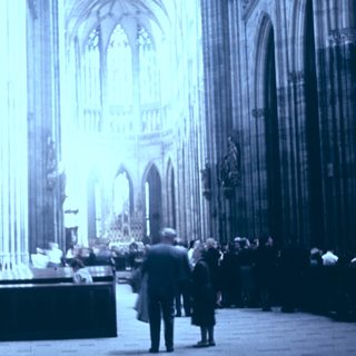 Gothic cathedral interior with visitors and stained glass.