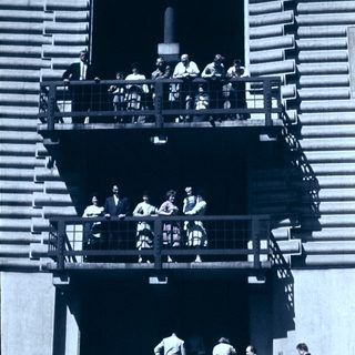 Group of people on outdoor balcony stairs, mid-20th century.