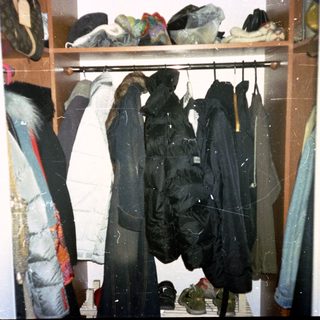 Cluttered closet with hanging jackets and folded clothes.