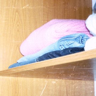 Cluttered closet with hanging clothes and folded items.