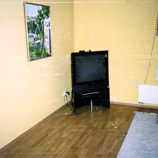 Empty room with old TV, damaged floor, and minimal furnishings.