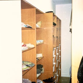 Cluttered wooden closet with folded clothes and shoes.