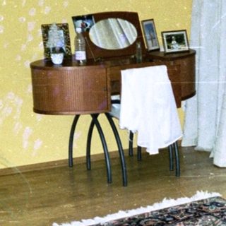 Mid-century bedroom with patterned rug, potted plant, desk, and balcony.