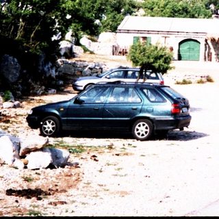 Rural roadside with mountain, small building, parked cars, and two people leading donkeys.