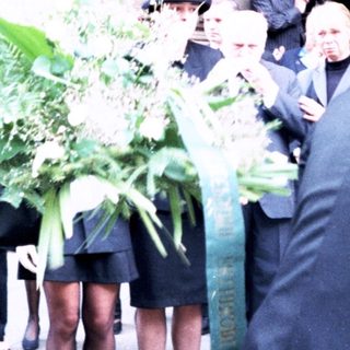 Formal gathering with floral tributes outside building.