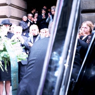 Formal gathering with floral tributes outside building.