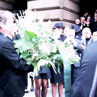 Formal gathering with floral tributes outside building.