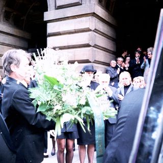 Formal gathering with floral tributes outside building.