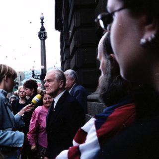 Public gathering with elderly man speaking to crowd near Nelson's Column.