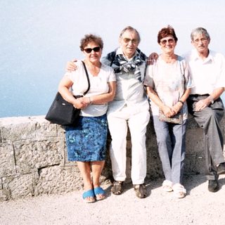 Four adults posing together outdoors by a stone wall.