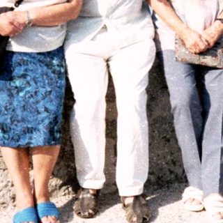 Four adults posing together outdoors by a stone wall.