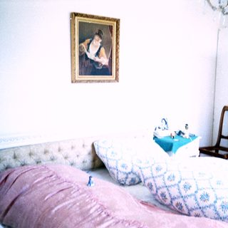 Classic bedroom with vintage bedding, framed portrait, and wooden furniture.