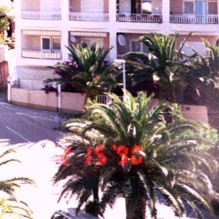 Sunny coastal town with Mediterranean-style buildings and mountains.