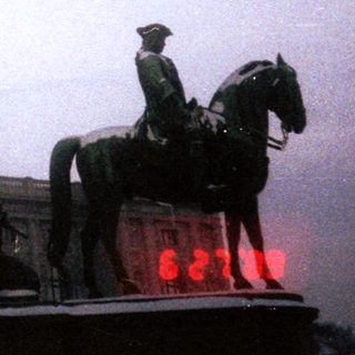 Equestrian statue with historical figures, illuminated at night.