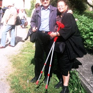 Elderly couple walking outdoors with mobility aid.