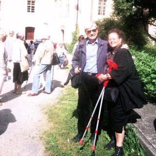 Elderly couple walking outdoors with mobility aid.