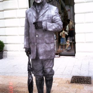Bronze statue of a man in vintage suit holding umbrella.