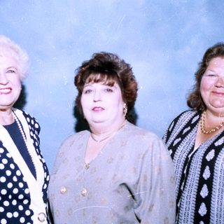 Three women posing together in formal attire.