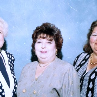 Three women posing together in formal attire.