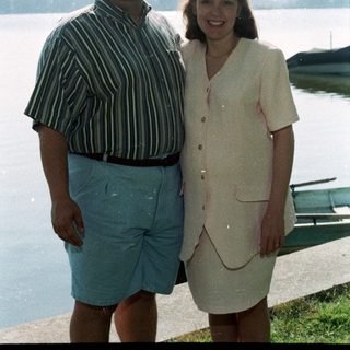 Two people smiling by a lake.