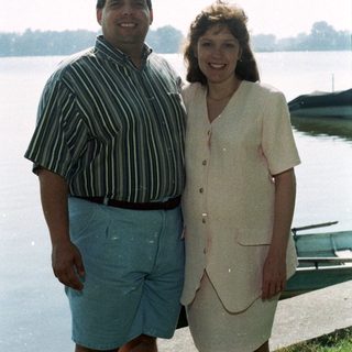 Two people smiling by a lake.