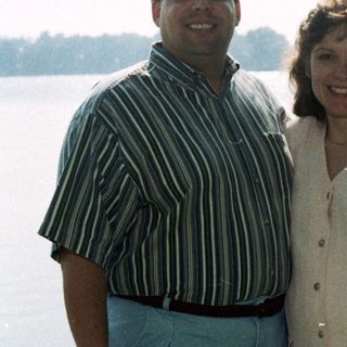 Two people smiling by a lake.