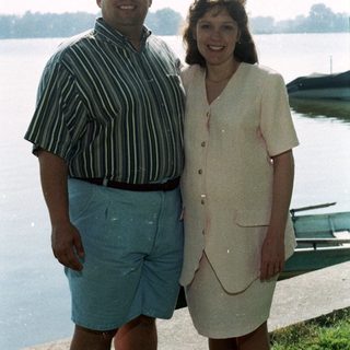 Two people smiling by a lake.