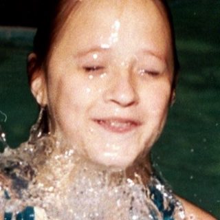 Girl joyfully splashing water in swimming pool.