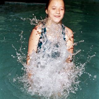 Girl joyfully splashing water in swimming pool.