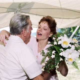 Joyful older man hugging woman holding bouquet.