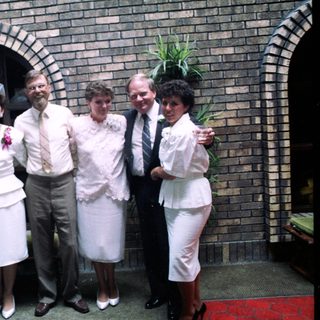 Group of seven people in 1970s-80s attire posing outdoors.