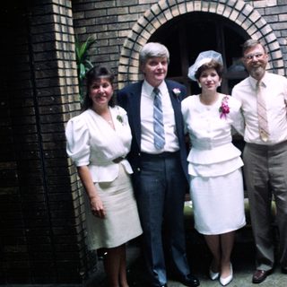 Group of seven people in 1970s-80s attire posing outdoors.