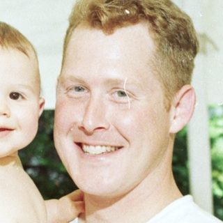 A man holding a smiling toddler outdoors.