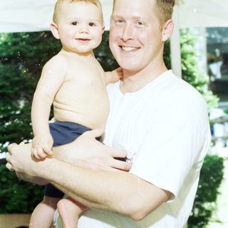 A man holding a smiling toddler outdoors.