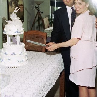 Couple cutting wedding cake indoors.