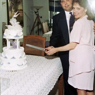 Couple cutting wedding cake indoors.