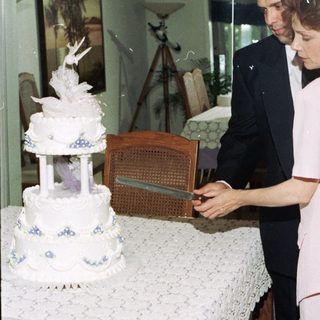 Couple cutting a multi-tiered wedding cake indoors.