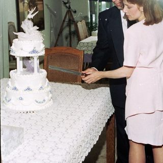 Couple cutting a multi-tiered wedding cake indoors.
