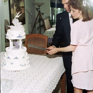 Couple cutting a multi-tiered wedding cake indoors.