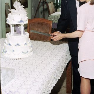 Couple cutting a multi-tiered wedding cake indoors.